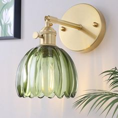 a green glass light fixture mounted on the side of a wall next to a potted plant