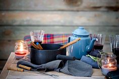 a table topped with glasses and pots filled with liquid next to candles on top of a wooden table