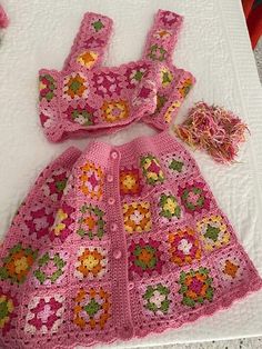 a pink crocheted dress and matching hat are laying on a white tablecloth