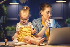 a woman and child sitting in front of a laptop computer while holding a pen and looking at the screen