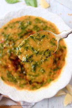 a spoon full of soup on top of a white bowl filled with sauce and spinach