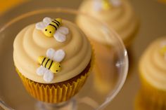 cupcakes with frosting and bees on them sitting on a glass plate in front of other cupcakes