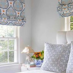 a bedroom with blue and white bedding, window shades and pillows on the headboard