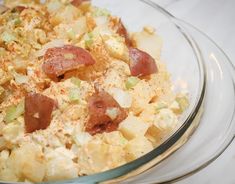 a glass bowl filled with potato salad on top of a white tablecloth covered table