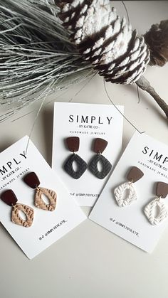 three small wooden earrings sitting on top of a card next to a pine cone and needles