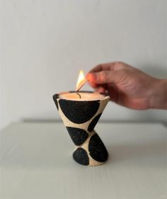 a person lighting a candle in a small black and white vase with geometric designs on it