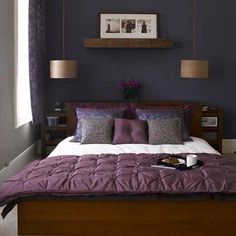 a bed with purple comforter and pillows in a bedroom next to two lamps on either side of the bed