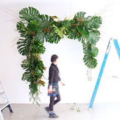 a woman walking past a green plant hanging from a ceiling in front of a white wall