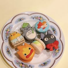 an assortment of decorated cookies on a plate with flowers and leaves around the edges, sitting on a table