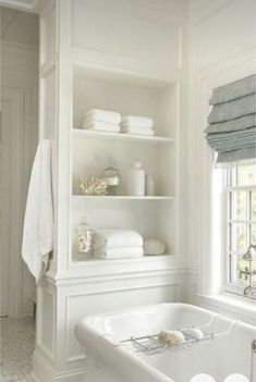 a white bathtub sitting next to a window filled with towels and other bathroom accessories