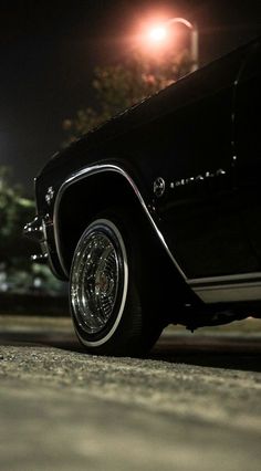 an old black car is parked on the street at night