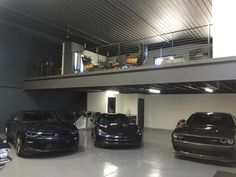 three cars are parked in a garage with two people standing on the second floor above them