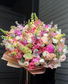 a woman holding a bouquet of flowers in front of a black door with pink, green and white flowers