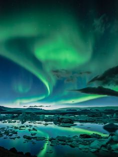 the aurora bore is glowing green in the night sky over ice floes and water