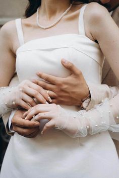 a woman in white dress holding another woman's hand with pearls on her arm