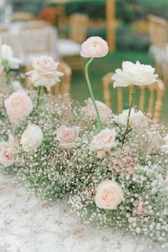 pink and white flowers are arranged in vases on a table with chairs behind them