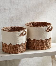 two woven baskets sitting on top of a wooden shelf next to a white wall, one with scalloped edges