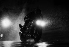 black and white photo of man on motorcycle in the rain at night with two headlights