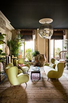 a living room filled with lots of furniture and plants on top of wooden flooring