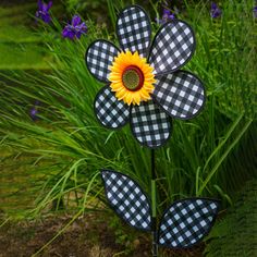 a sunflower is sitting in the middle of some grass and purple flowers are behind it