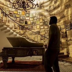 a man standing next to a grand piano in front of a staircase with pictures on the wall