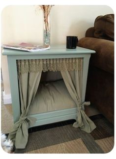 a dog bed with curtains on top of it and a vase filled with flowers next to it