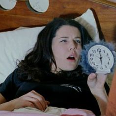 a woman laying in bed with an alarm clock next to her face and mouth open