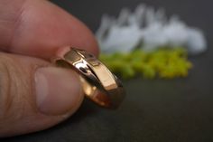 a hand holding a gold wedding ring next to some flowers