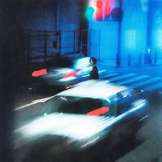 blurry photograph of cars driving down the street at night time with traffic lights on