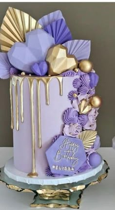 a purple and gold birthday cake with decorations on the top is sitting on a table