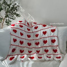 a white crocheted blanket with red hearts on it sitting on top of a bed