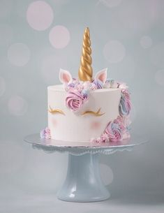 a white cake with pink and blue frosting has a unicorn horn on top, sitting on a pedestal