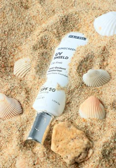 a tube of sunscreen on the sand with seashells