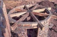 an old water wheel is sitting in the middle of some dirt and rocks with wood bars around it