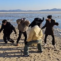 several people are dancing on the beach by the water with their hands in the air