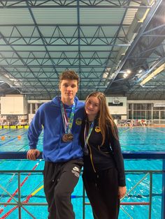 two people standing next to each other in front of a swimming pool with medals on their necks