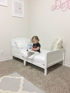 a toddler sitting on a white bed reading a book in her room with the word best written above it