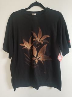 a black t - shirt with gold flowers on it hanging from a hanger against a white wall