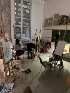 an artist's studio with easels and paintings on the walls, two people sitting at their desks