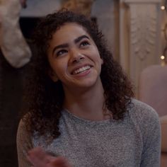 a woman with curly hair is smiling and looking up at the camera while wearing a gray sweater