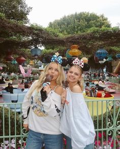 two women standing next to each other in front of an amusement park