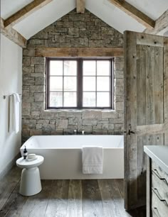 a bathroom with a stone wall and wooden flooring that has a white bathtub in it