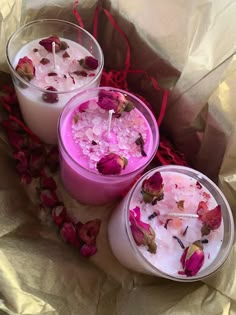 three candles with rose petals on them sitting next to each other in front of some tissue paper