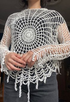 a woman wearing a white crochet top with long sleeves and an openwork design