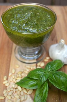 pesto sauce in a glass bowl with basil leaves and garlic on a wooden cutting board