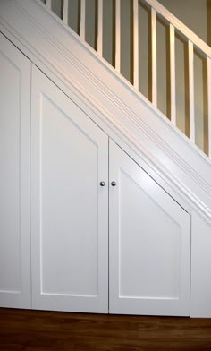 an under the stairs storage area with white cupboards and wood flooring in a home