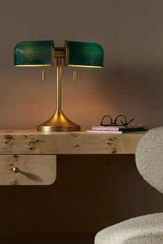 a table with a lamp and some books on it next to a chair in front of a wall