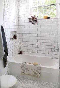 a white tiled bathroom with a tub and toilet