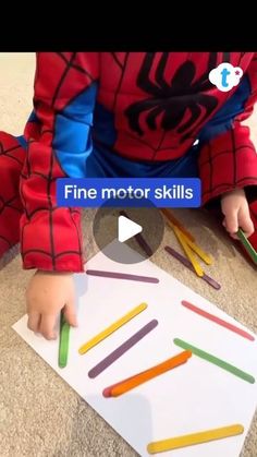 a toddler is playing with colored pencils on the floor in front of a spiderman cutout