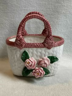 a white basket with pink flowers and green leaves on the inside is sitting on a table